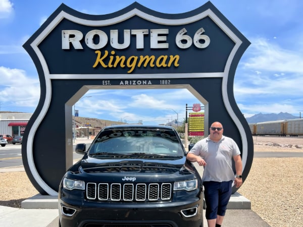 Michael Blass steht neben einem Mietwagen vor dem Route 66 Schild in Kingman, Arizona