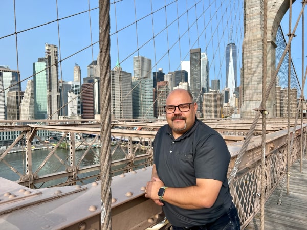 Michael Blass steht auf der Brooklyn Bridge vor der Skyline von Manhattan